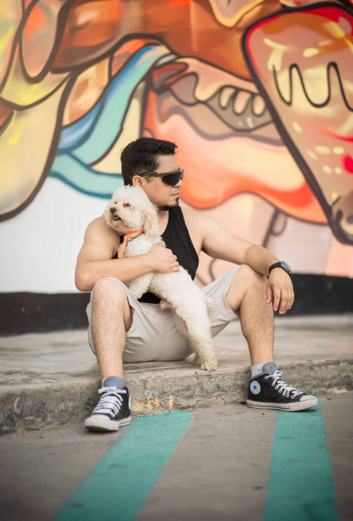Un hombre sosteniendo un perro frente a un muro de graffiti.