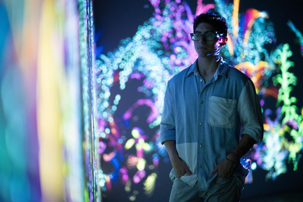 Un hombre parado frente a una pared con luces de colores en una galería de arte.